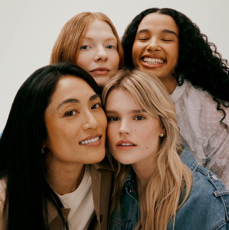 Four women with different hair types posing together in front of a plain background.