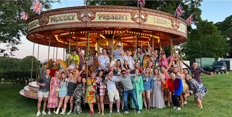 company photo of all the employees at the CLOUD NINE carnival with a horse carousel in the background 