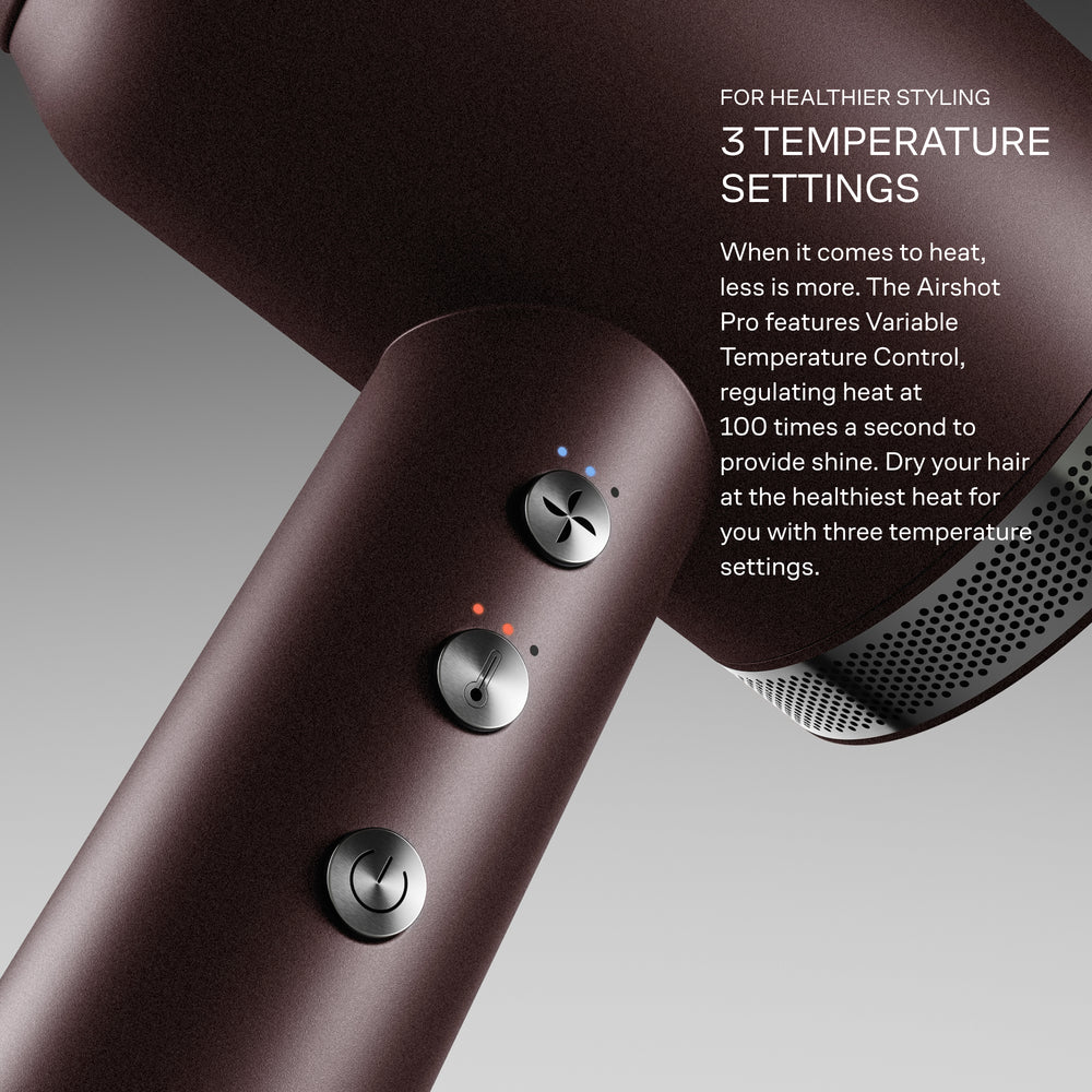 Hair dryer with temperature control settings on a grey background. 'For healthier styling, 3 temperature settings. When it comes to heat, less is more. The Airshot Pro features Variable Temperature Control, regulating heat at 100 times a second to provide shine. Dry your hair at the healthiest heat for you with three temperature settings.'