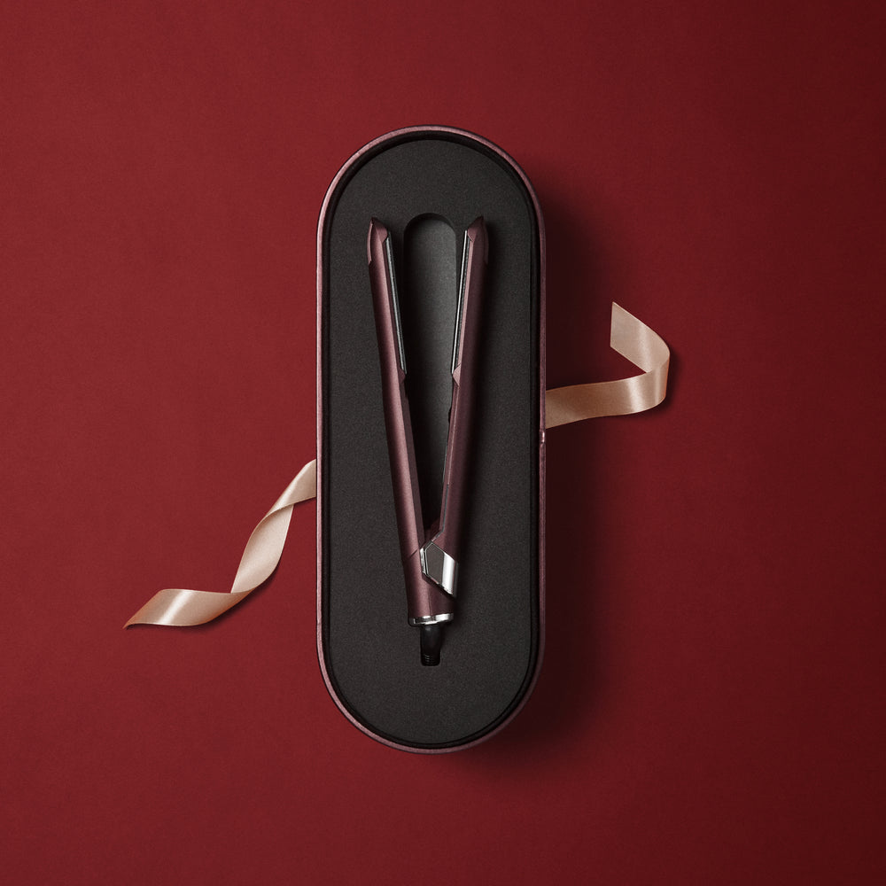 The Original Iron in a Dark Burgundy finish, laid on a matching case, displayed on a red background with a decorative pink bow.