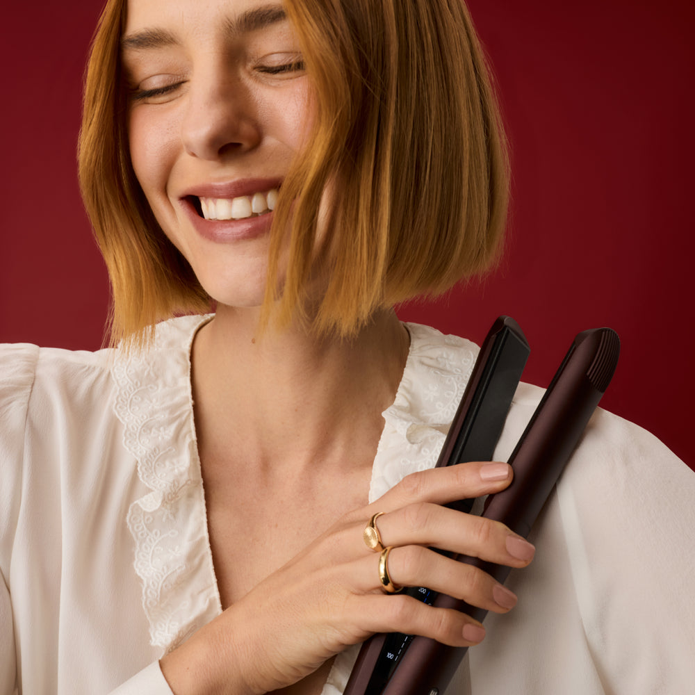 Smiling woman with a bob holding The Wide Iron in Dark Burgundy, in front of a red background.