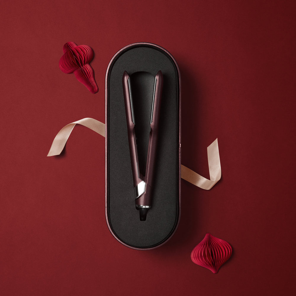 The Wide Iron in a Dark Burgundy finish, laid on a matching case, displayed on a red background with decorative festive ornaments and a pink bow.