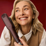 Blonde-haired woman holding The Wide Iron in Dark Burgundy, in front of a red background.
