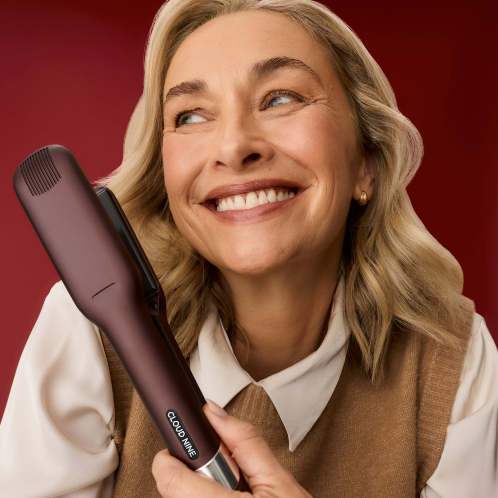 Blonde-haired woman holding The Wide Iron in Dark Burgundy, in front of a red background.