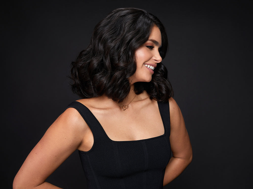Model with short dark curled hair, smiling and looking away from the camera.