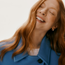 Woman with red hair, smiling and wearing a blue coat against a neutral background.
