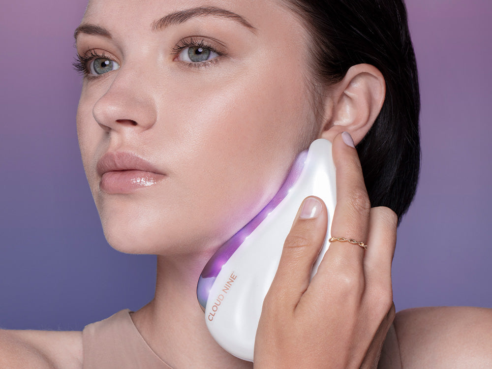 Female model holds the Redefine beauty device to jawline with Purple Light activated.