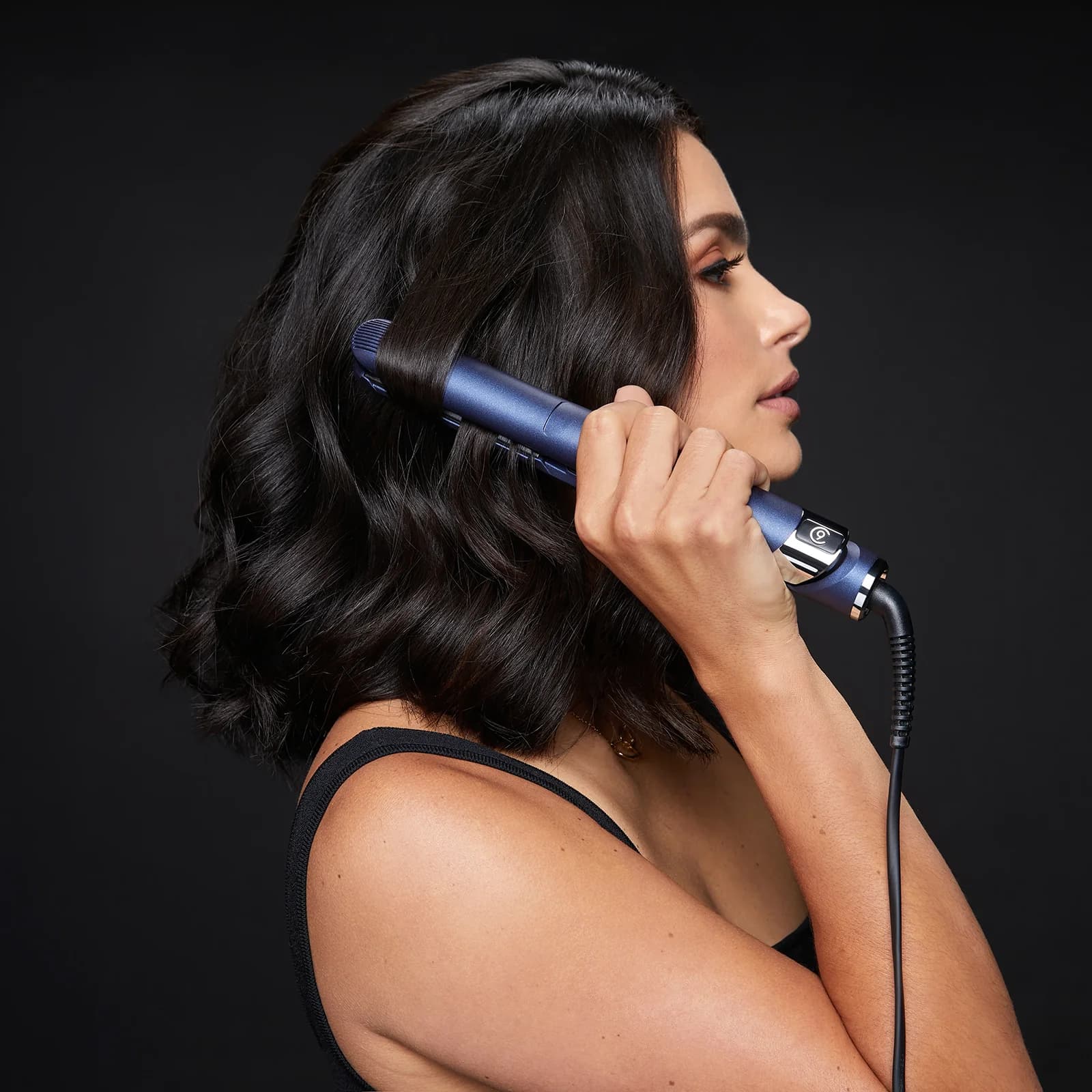 side view of female model with jet black short wavy hair holding 2-in-1 Contouring Iron Pro in hand while straighteneing her hair