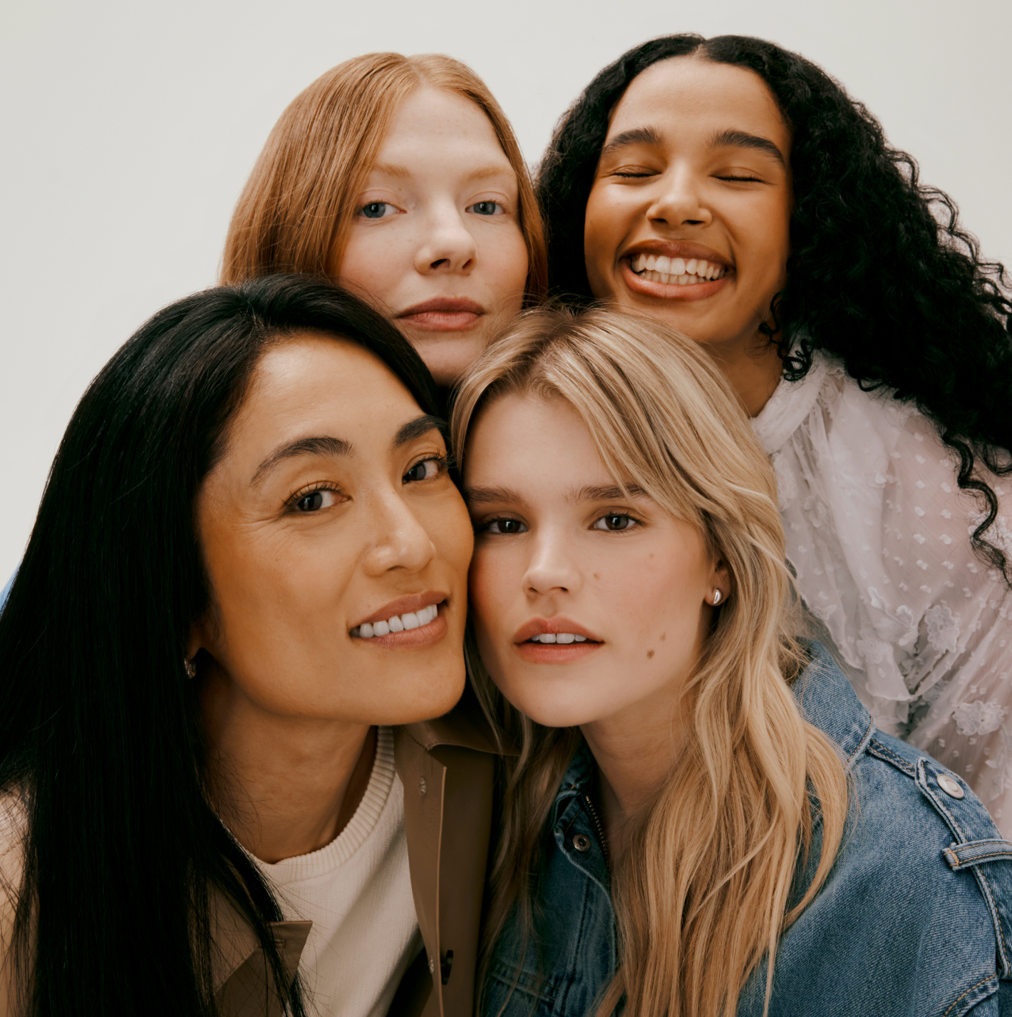 Four women with different hair types posing together in front of a plain background. 